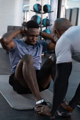 Personal trainer coaching male client doing sit-ups on mat in modern gym