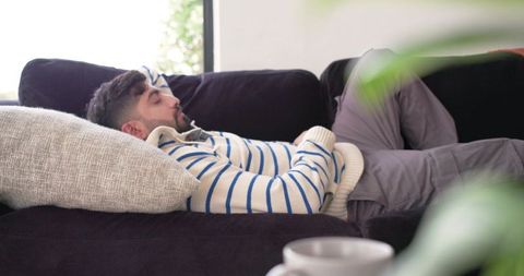 Indian man lying on couch resting in cream striped sweater with pillow and coffee mug