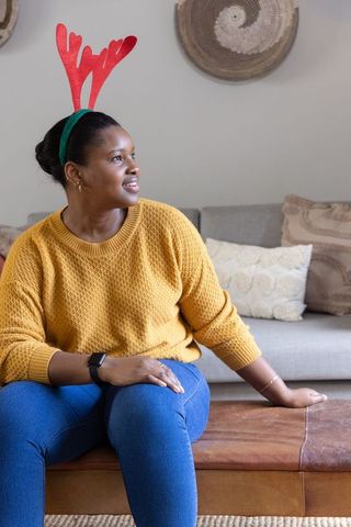 African american woman wearing red antler headband and yellow sweater sitting on couch