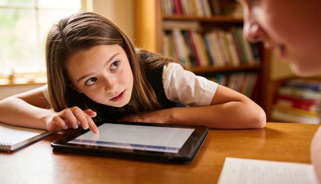 Curious student leaning on desk pointing at tablet during sunlit home tutoring session