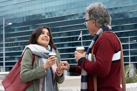 Hispanic couple sharing playful coffee conversation on urban terrace with takeaway cups