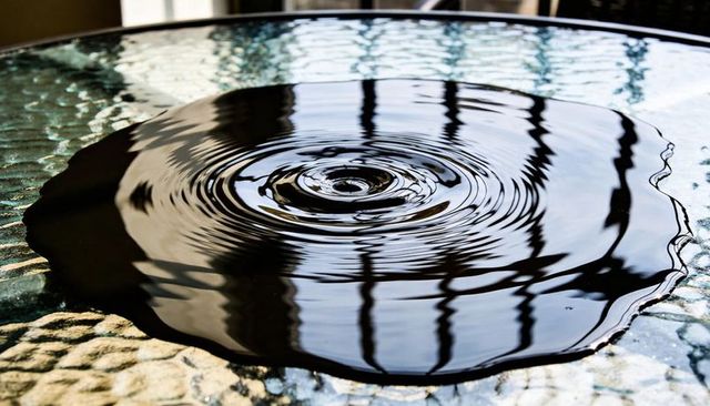 Concentric ripples creating bold reflections on textured glass table with vertical bars