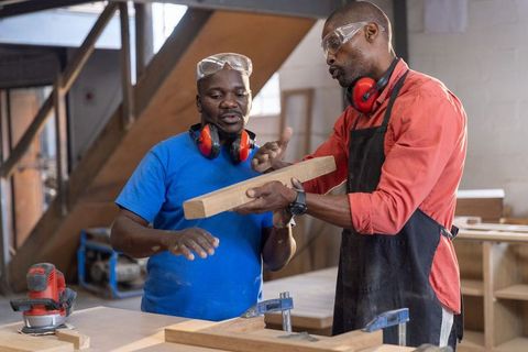 African american mentor teaching apprentice woodworking techniques in carpentry workshop