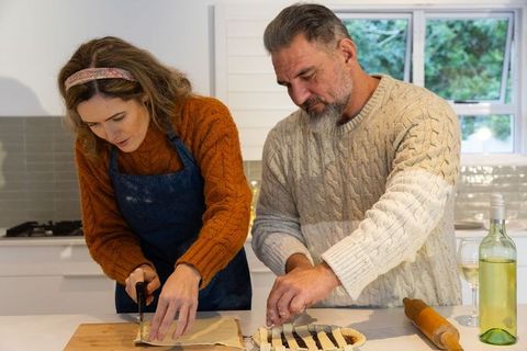 Middle-aged couple assembling lattice pie cutting pastry on kitchen counter cozy baking