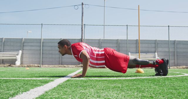 Disabled biracial male football player, doing push-ups on outdoor pitch. Football, sports, fitness, disability and inclusivity.