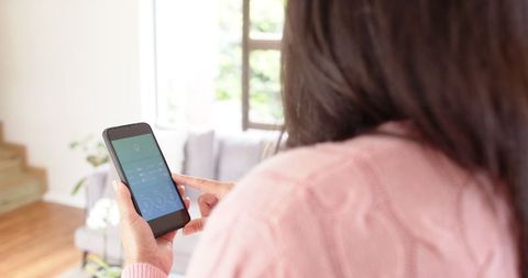 Woman using smartphone for smart home control in cozy living room