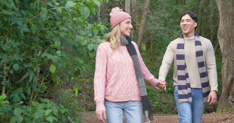 Couple walking hand-in-hand on woodland trail wearing cozy knit sweaters and scarves