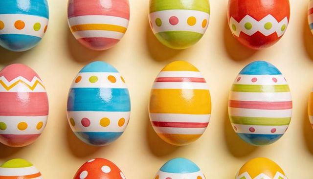 Glossy hand-painted striped Easter eggs arranged in colorful grid on pale yellow tabletop
