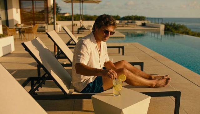 Man relaxing at infinity pool stirring lemon cocktail on seaside villa terrace