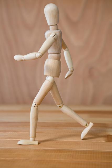 Wooden mannequin depicted in a walking posture on a wooden floor. This can be used in art classes, design presentations, or creative projects to symbolize movement, creativity, or simplicity. Suitable for illustrating concepts of motion and artistic expression.