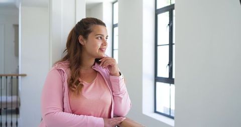 African woman leaning on banister looking out bright windows in contemporary home