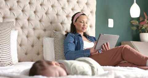Relaxed hispanic mother using tablet while infant sleeps