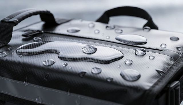 Black water-resistant messenger bag with beading droplets on carbon-fiber texture