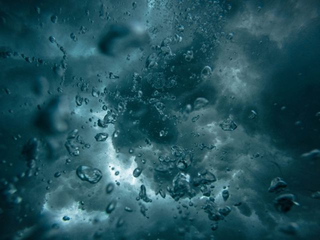 Underwater view with bubbles rising against a dark, dramatic backdrop. Ideal for illustrating concepts of the ocean, aquatic life, or underwater mysteries. Suitable for use in environmental themes, stormy or turbulent scenes, and educational material about the deep sea.