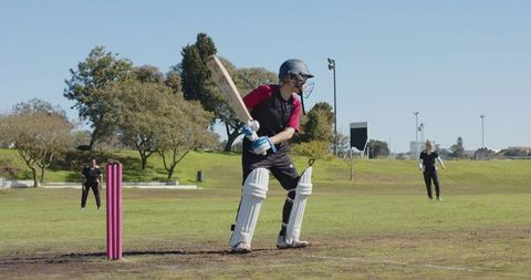 Female Cricketer Batting on Pitch with Teammates Fielding