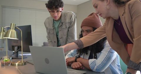 Diverse young professionals collaborating over laptop during modern office meeting