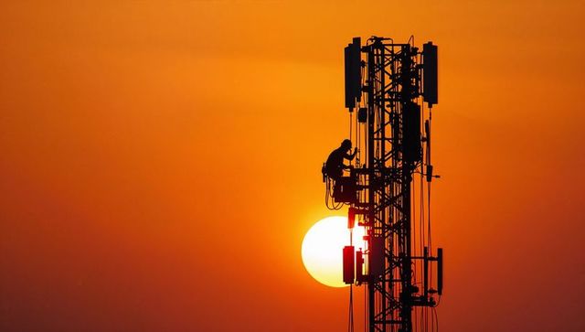 Silhouetted telecom technician climbing tower at sunset