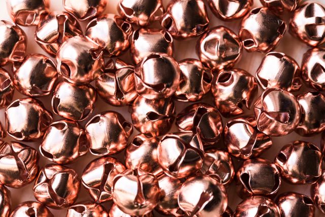 Shiny copper bells arranged in a close-up view, showing their reflective surfaces and detailed textures. The image highlights the charm and appeal of metallic decorations typically used during festive holidays such as Christmas. Ideal for use in holiday cards, festive event flyers, seasonal craft ideas, or as a visual element in gift wrapping and ornament projects.