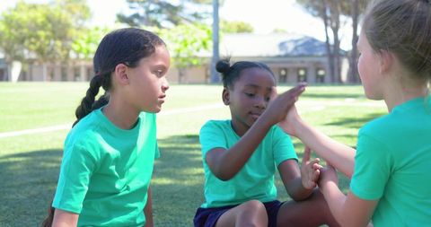 Girls playing clapping game on school field wearing green shirts, teamwork and friendship