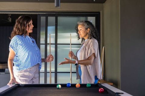 Multiracial women playing pool and chatting in modern home lounge over friendly game