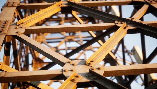Sunlit steel lattice tower close-up showing beams, gusset plates and bolted truss geometry