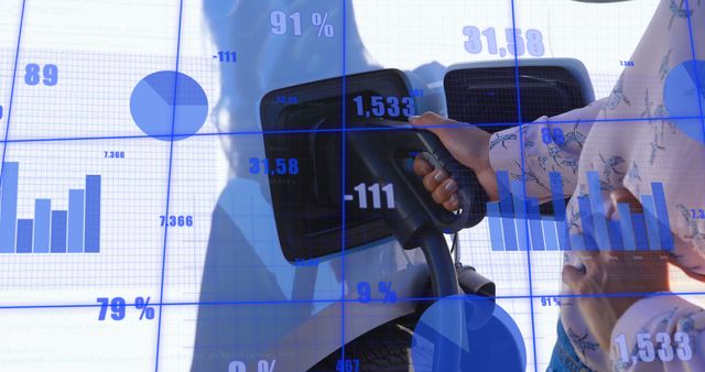 Shows hand holding an EV charger at an electric vehicle charging station. Blue financial charts and graphs overlaying the scene symbolize the intersection of green technology and market data. Perfect for use in articles or presentations on sustainable energy developments, investment opportunities in green technology, or future of electric vehicles.