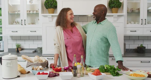 Image of happy diverse female and male senior friends preparing meal in kitchen, embracing. retirement lifestyle, spending quality time with friends.