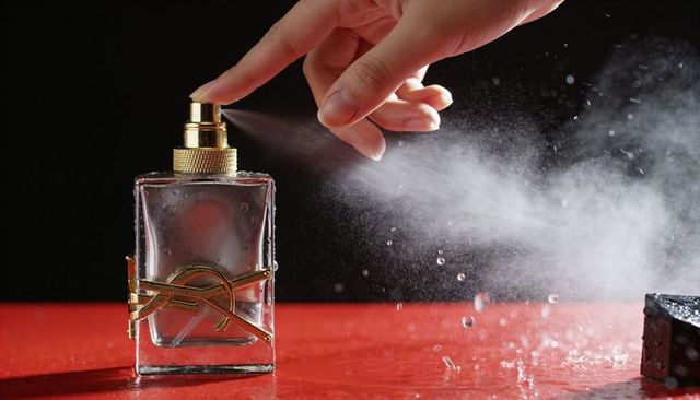 Luxury perfume spray releasing fine mist from gold atomizer over glossy red surface