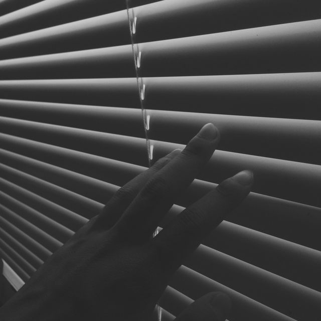 This image shows a hand partially opening window blinds, allowing light to filter through. This photo is perfect for concepts related to privacy, control, or daily routines. Useful in articles, blogs, or advertisements focusing on home interiors, personal space, or morning activities.