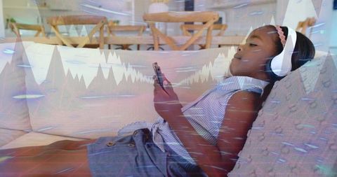 Relaxing girl listening to music with headphones and using smartphone on sunlit sofa