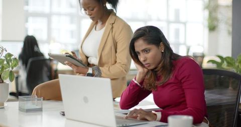 Black and South Asian Coworkers Collaborating on Laptop and Tablet in Modern Open Office