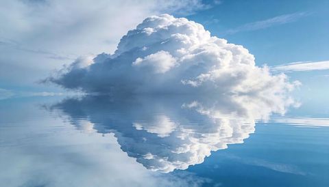 Towering cumulus cloud reflecting perfectly over glassy lake, minimalist blue cloudscape