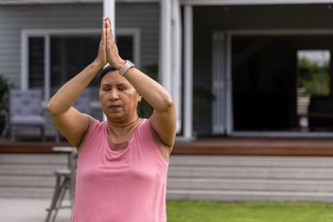 Mature woman practicing yoga in backyard wearing pink top and fitness tracker