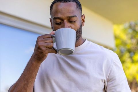 Mature african american man sipping coffee on porch with ribbed mug, morning routine