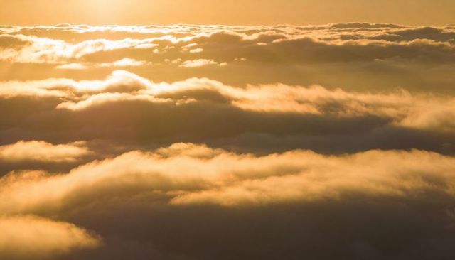 Golden sunrise bathing layered cloud deck in warm light above high-altitude horizon