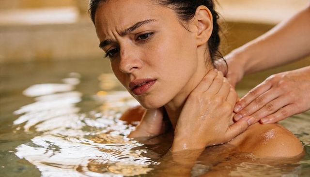 Woman receiving neck and shoulder massage in thermal therapy pool, closeup spa moment