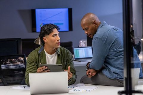 Diverse male coworkers discussing data on laptop and tablet in modern office