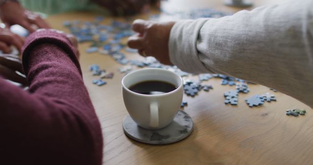 Hands of group of diverse senior friends drinking coffee and doing puzzle at home. socialising with friends at home.
