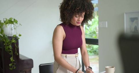 Woman standing at desk reviewing documents in modern home office with natural light
