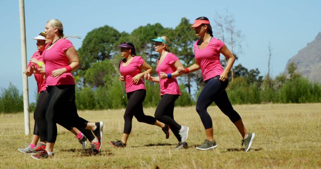 Group of women running together wearing matching pink t-shirts and sports caps. Ideal for fitness, exercise, and active lifestyle themes. Suitable for wellness and teamwork concepts, as well as promoting outdoor activities and healthy living.