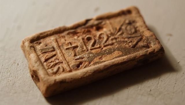Weathered terracotta seal showing carved glyphs and dust on textured tabletop, macro closeup