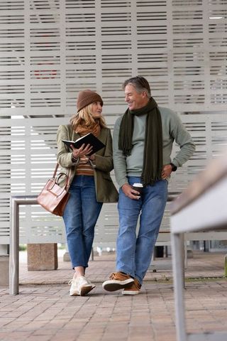 Middle-aged couple sharing coffee and notebook at urban transit shelter, casual autumn style