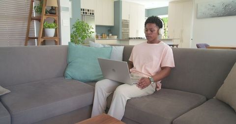 Young man working remotely on laptop wearing headphones in modern open-plan living room