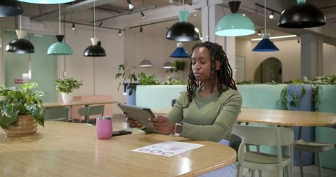 Young woman working on tablet in pastel coworking space with charts, plants, modern lamps