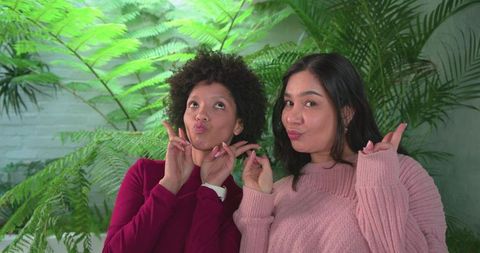 Two women posing, puckering lips and playing with fingers in lush botanical greenhouse