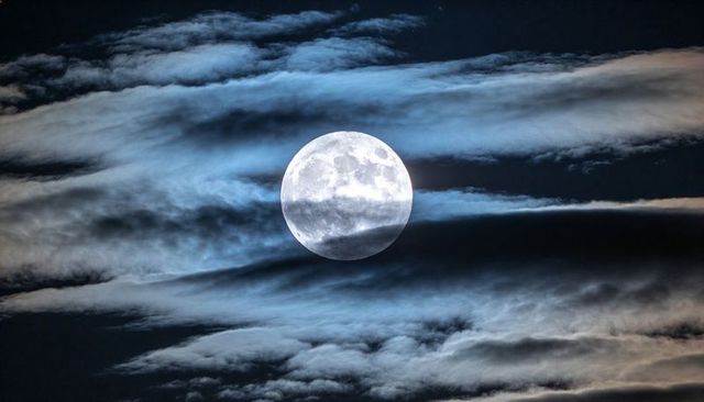Full Moon Illuminating Layered Clouds and Cratered Lunar Surface in Night Sky