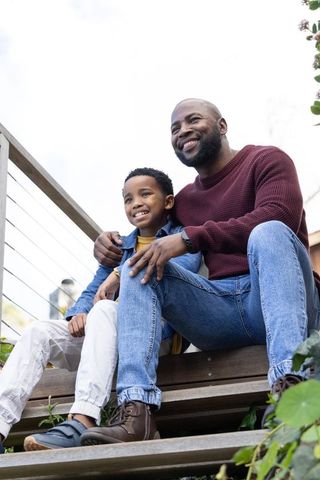 African american father holding son on wooden steps, smiling and bonding outdoors