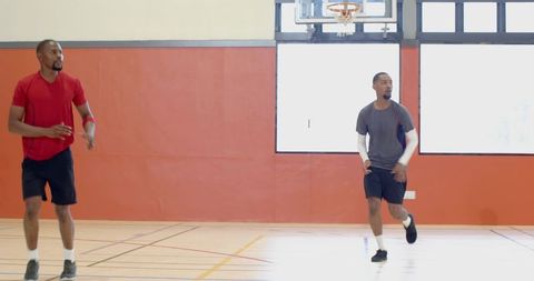 Two men practicing basketball drill on bright indoor court with hoop and hardwood floor
