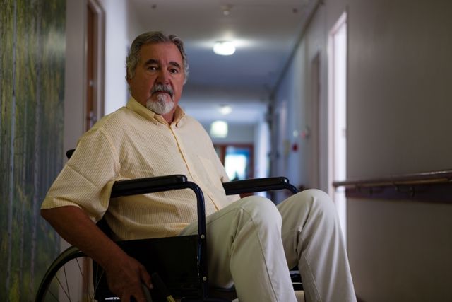 Senior man sitting in a wheelchair in a corridor of a retirement home. This image can be used for topics related to elderly care, healthcare facilities, aging, disability support, and independent living for seniors.