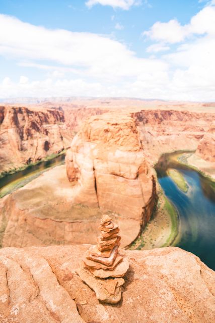 Stacked stones on edge of cliff with Horseshoe Bend in background. Perfect for travel blogs, nature enthusiasts, motivational quotes, or adventure travel promotions.